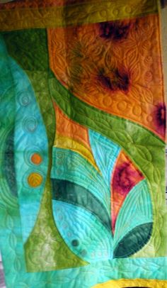 a quilted wall hanging on the side of a building with an abstract design in green, orange and yellow