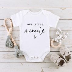 a white baby bodysuit with the words our little miracle on it next to shoes and beads