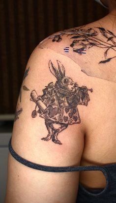 the back of a woman's shoulder with tattoos on her arm and an image of a rabbit