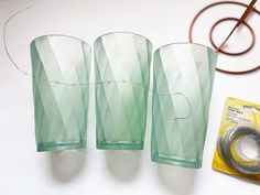 three green glass vases sitting on top of a table next to scissors and tape