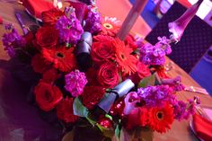 a bouquet of red and purple flowers sitting on top of a table next to plates