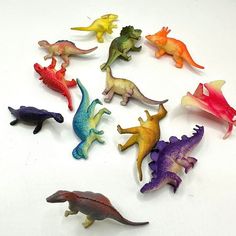 there are many small toy dinosaurs on the white table together, all different colors and sizes