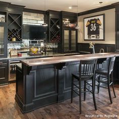 a large kitchen with black cabinets and an island in front of two bar stools