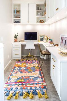 a white desk with a computer on top of it and a colorful rug in front of it