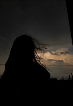 the silhouette of a woman with her hair blowing in the wind