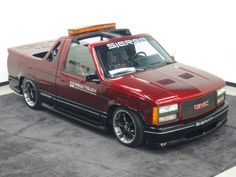 a red pick up truck parked on top of a black carpeted floor next to a white wall