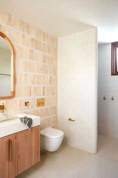 a white toilet sitting next to a wooden cabinet in a bathroom under a mirror on the wall