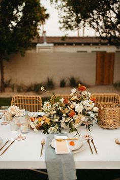 a table set with flowers and place settings for an outdoor dinner party in the backyard