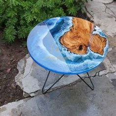 a small blue table with a wooden piece on it's side and some plants in the background