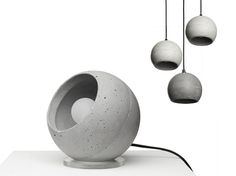 three concrete balls are suspended from wires on a white surface, and one is shaped like an egg