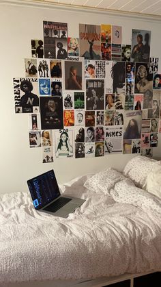 a laptop computer sitting on top of a bed covered in pictures and posters next to a window