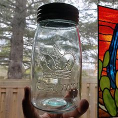 a hand holding a mason jar with a stained glass window behind it