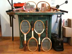 several tennis rackets are stacked on top of a green table in a room with hard wood flooring