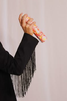 a woman in a black jacket is holding a pink and white object with fringes on it