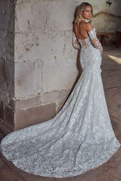 a woman in a wedding dress leaning against a stone wall with her back to the camera