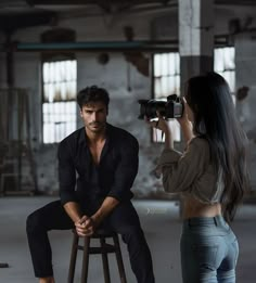 a man sitting on a stool next to a woman with a camera in her hand