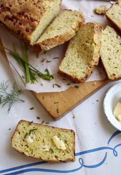 sliced loaf of bread with butter and herbs on cutting board next to bowl of butter