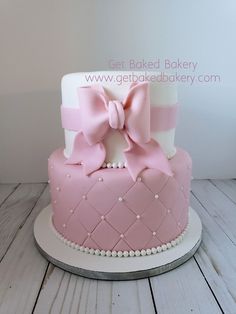 a pink and white cake with a big bow on it's top is sitting on a table