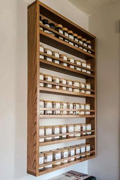 a wooden shelf filled with lots of jars on top of a white wall next to a window