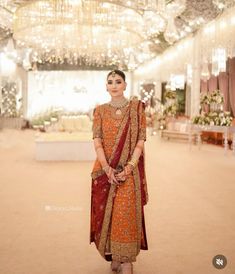 a woman standing in front of a chandelier wearing an orange and red outfit