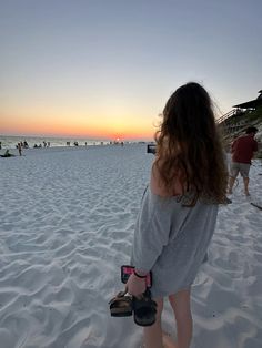 a woman standing on top of a sandy beach next to the ocean with people in the background