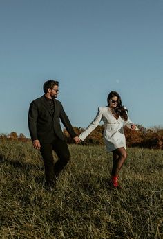 a man and woman holding hands walking through tall grass