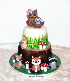 there is a cake decorated with animals and mushrooms on the tablecloth, along with an owl figurine