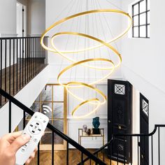 a person holding a remote control in their hand while standing next to a spiral chandelier