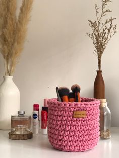 a pink crocheted basket sitting on top of a table next to bottles and flowers