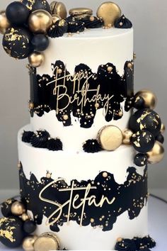 a white and black birthday cake with gold decorations on the top tier, decorated with confetti