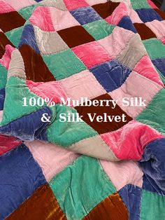 a bed with a pink, blue and green quilt on it's cover that says 100 % mulberry silk & silk velvet