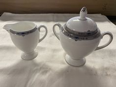 two white teapots sitting on top of a cloth covered table next to each other