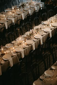 a long table is set with white plates and silverware for an elegant dinner party