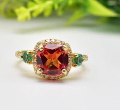 a ring with an orange and green stone surrounded by three emeralds on the side