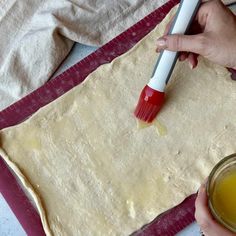 someone using a brush to make dough on a sheet of paper with orange juice in the foreground