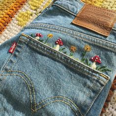 a pair of jeans with embroidered flowers and mushrooms on the back, sitting on a rug