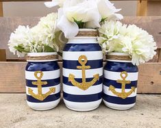 three blue and white striped mason jars with gold anchor decals on them, along with flowers