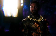 a man dressed in black and gold standing next to a wall with lights on it