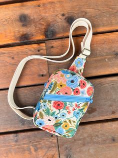 a multicolored floral cross body bag hanging on a wooden floor with a white strap