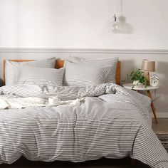 an unmade bed with striped sheets and pillows on top of it in a white room