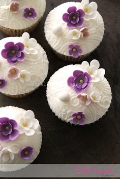 four cupcakes with white frosting and purple flowers