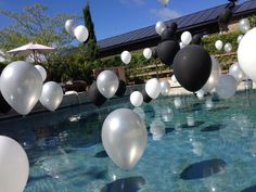 white and black balloons floating in the air over a pool with clear blue water below