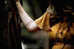 a woman with a tattoo on her arm leaning against a tree