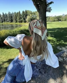 a woman sitting on top of a rock next to a tree wearing a bandana