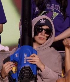 a woman with sunglasses and a hoodie holding a bat in front of her face