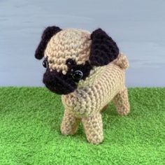 a small crocheted pug dog standing on green grass