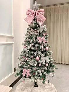 a small christmas tree with pink bows and ornaments on it's top, sitting in front of a window