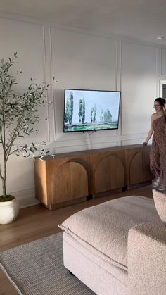 a woman standing in front of a flat screen tv on a wall mounted above a wooden cabinet