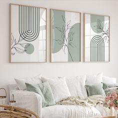 three paintings hang on the wall above a white couch with pillows and flowers in vases