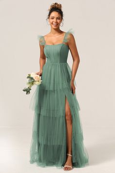 a woman in a long green dress holding a bouquet and posing for the camera with her legs crossed